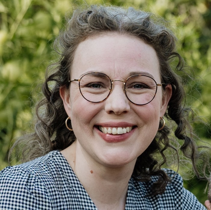 Headshot of Aleithia Stephens, a white woman with curly brown hair and round wire-rimmed glasses